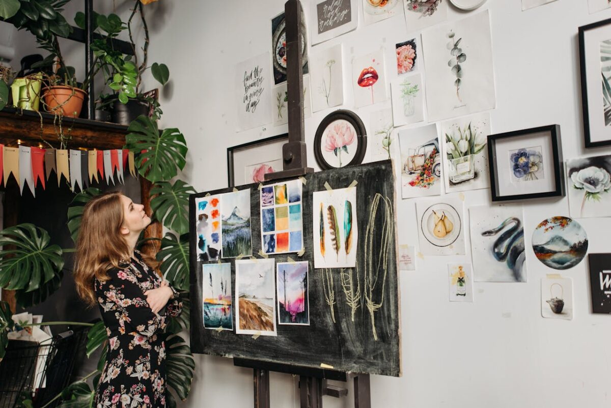 A young woman in a floral dress admires a collection of artwork in a creative studio setting.