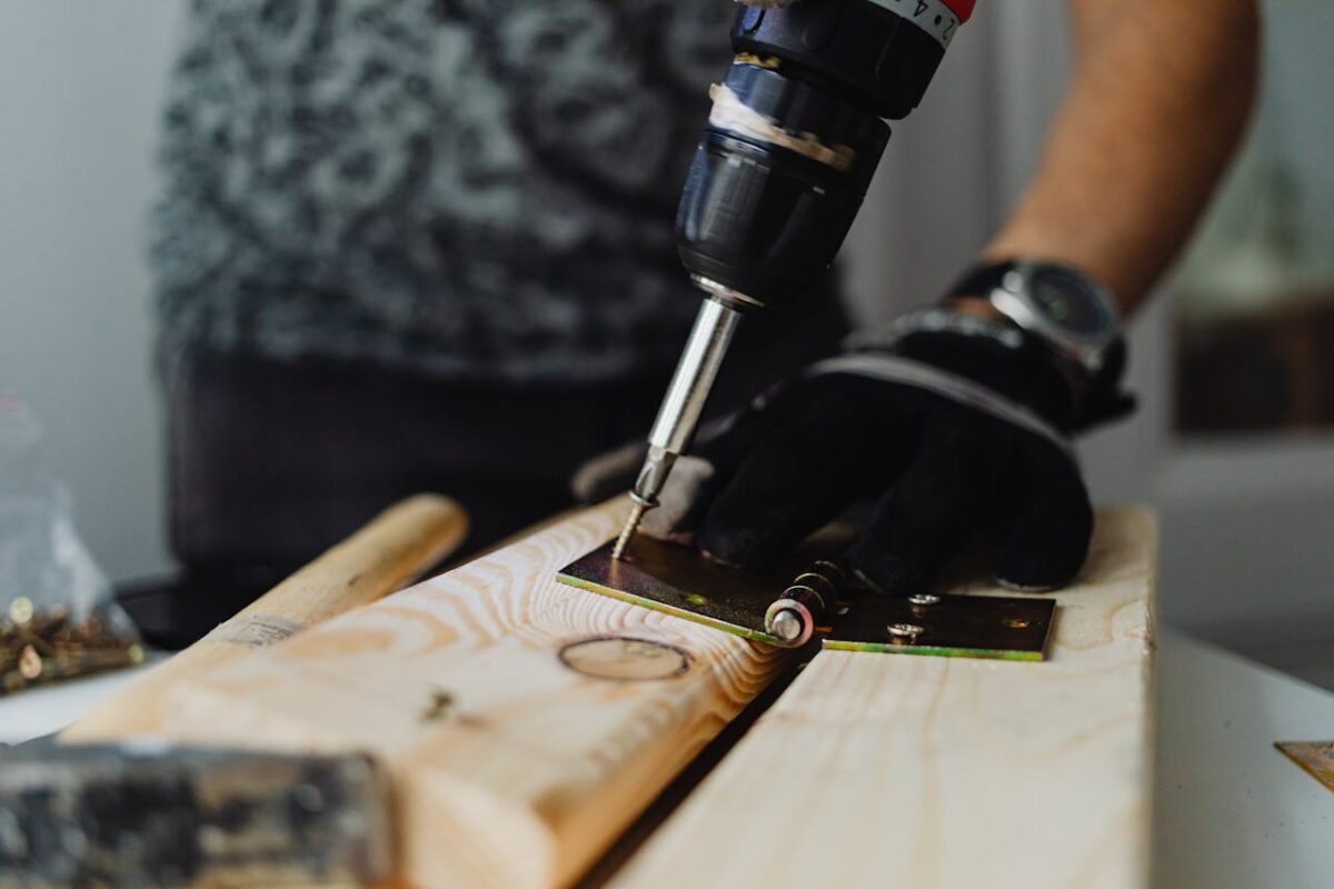 Focused close-up of a handyman using a drill on a wooden plank indoors.