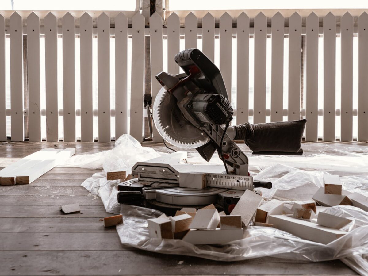 A circular saw on a wooden terrace with cut wood pieces and a white fence.