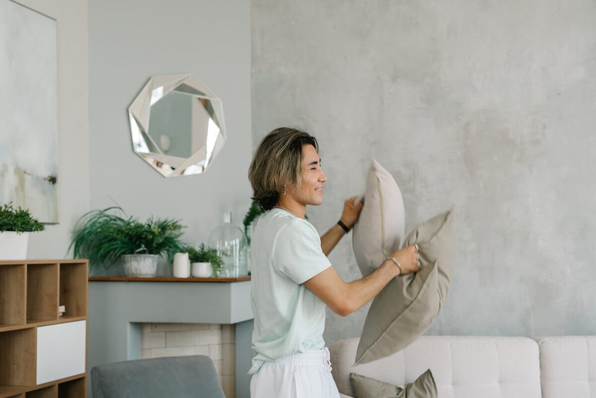 A young adult arranges pillows in a stylish, modern living room setting.